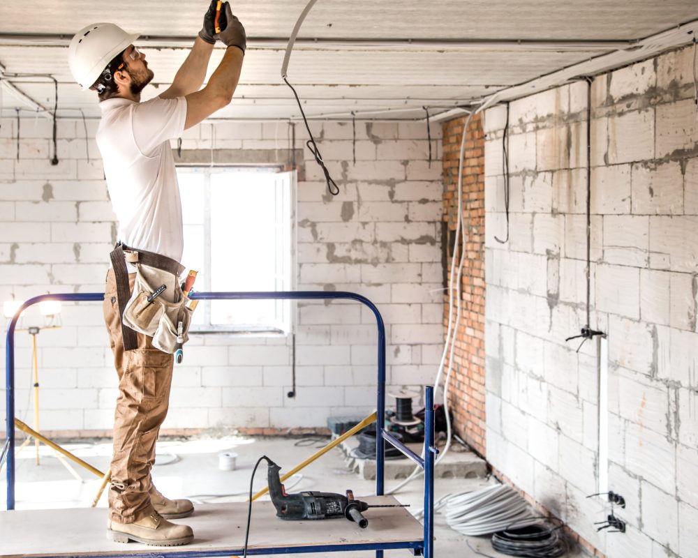 Electrician installer with a tool in his hands, working with cable on the construction site. Repair and handyman concept. House and house reconstruction.